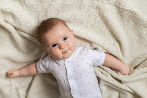 Portret van schattige pasgeboren baby in lichte kleding liggend op grijze linnen sprei producten voor kinderen