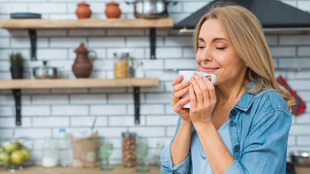 Foto portret van schitterende glimlachende dame die en koffie van kop in de keuken ruiken drinken