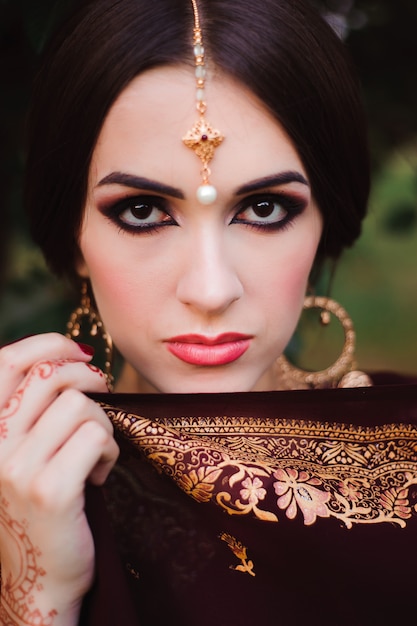 Portret van schoonheid indiase model met lichte make-up die haar gezicht achter de sluier verbergt. jonge hindoe vrouw met mehndi tatoeages van zwarte henna op haar handen