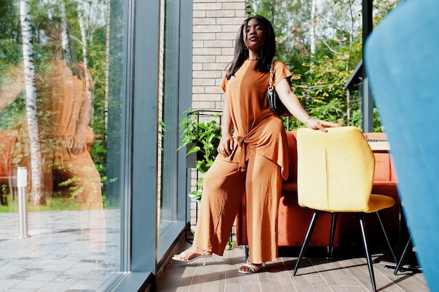 Portret van schoonheid jonge zwarte vrouw, oranje outfit dragen, poseren in restaurant.