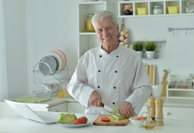 Portret van senior man in de keuken met laptop thuis