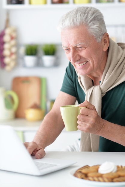 Portret van senior man in de keuken thuis met laptop