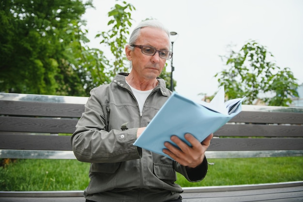 Portret van senior man lezen op bankje tijdens zomerdag