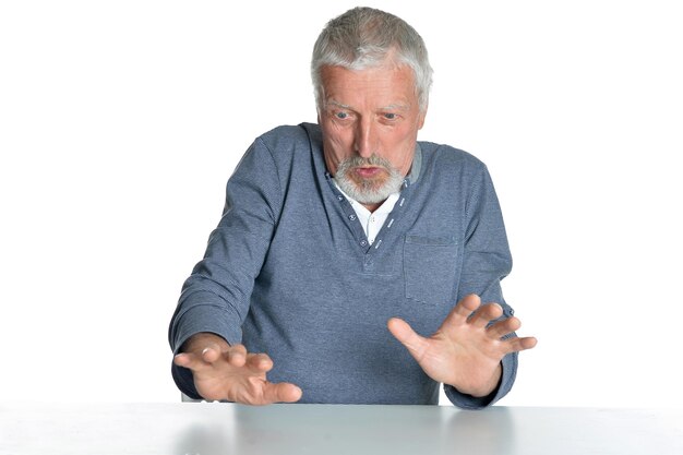 Portret van senior man zit aan tafel geïsoleerd op witte achtergrond