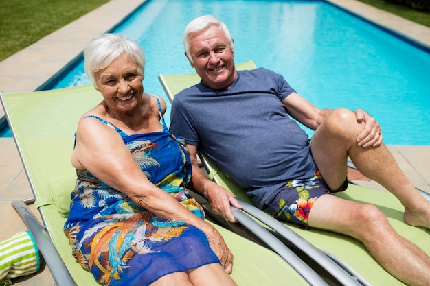 Portret van senior paar ontspannen op luie stoel bij zwembad