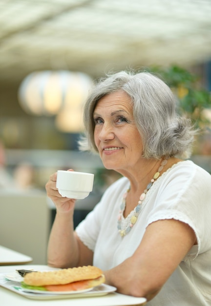 Portret van senior vrouw met kopje koffie en sandwich