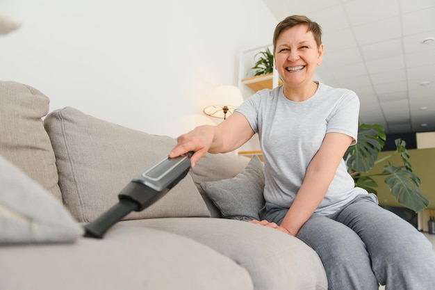 Portret van senior vrouw met stofzuiger binnenshuis thuis stofzuigen