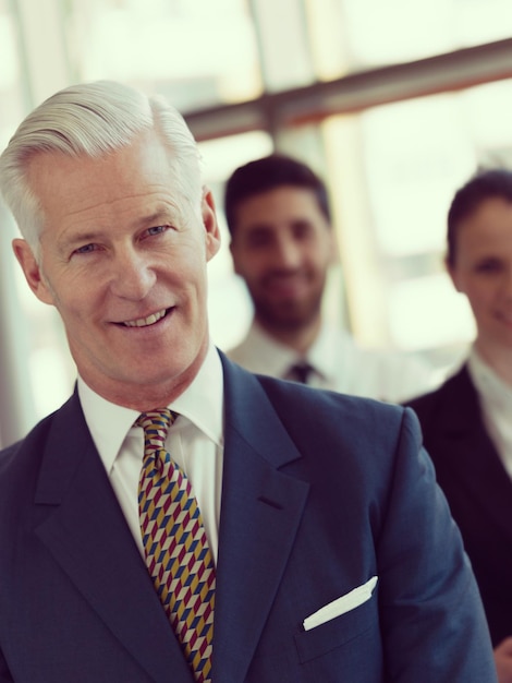 Foto portret van senior zakenman als leider bij modern, helder kantoor, zakelijke teammensengroep op achtergrond