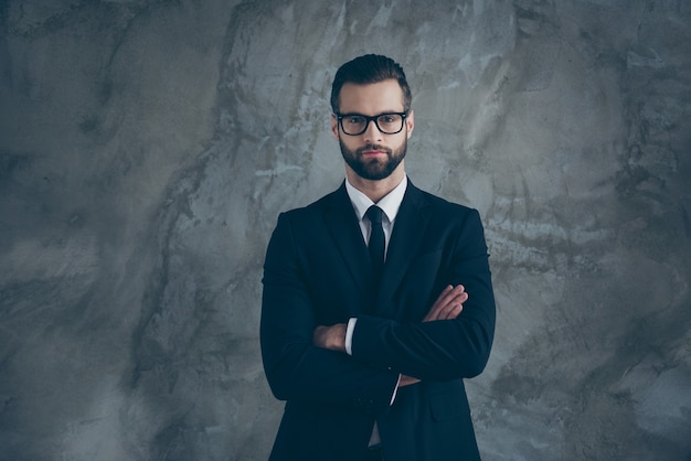 Portret van serieuze geconcentreerde kerel werknemer werk in grote grote onderneming kruis handen klaar beslissen beslissing kiezen keuze dragen stijlvol pak zwarte baan kleding geïsoleerd over grijze kleur muur