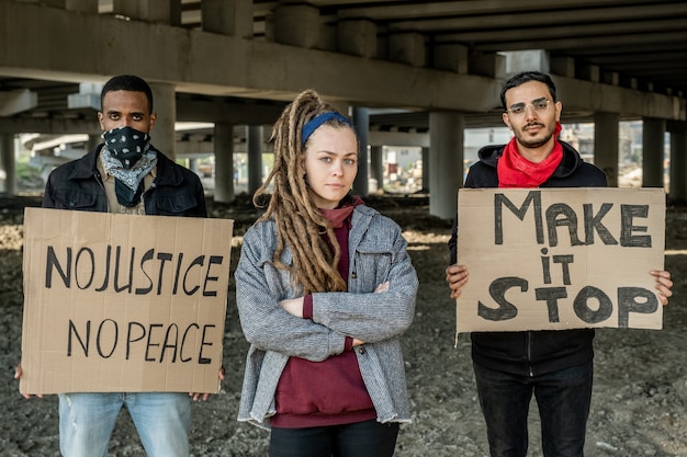 Portret van serieuze jonge interraciale mensen die met borden onder de brug staan terwijl ze deelnemen aan een demonstratie