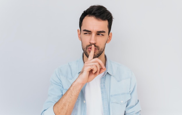 Portret van serieuze modieuze man gekleed trendy in blauw shirt houdt voorvinger op de lippen shh gebaar maken voor geheim of stil zijn geïsoleerde schot van stijlvolle man toont stilte teken mensen concept