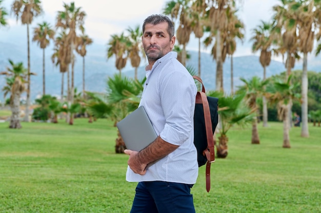 Portret van serieuze zelfverzekerde volwassen man met laptop buitenshuis