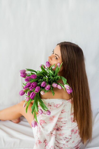 Portret van sexy mooie jonge vrouw met lang haar Model met een boeket lila tulpen op wit Voorjaarsvakantie