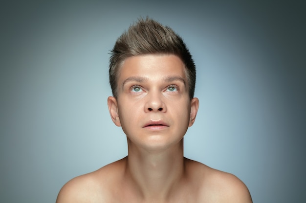Portret van shirtless jonge man geïsoleerd op een grijze muur. Kaukasisch gezond mannelijk model opzoeken en poseren. Concept van de gezondheid en schoonheid van mannen, zelfzorg, lichaams- en huidverzorging.