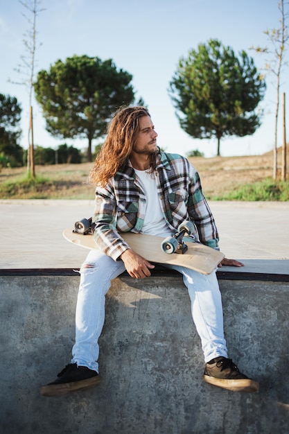 Portret van skater zittend op de rand van het zwembad terwijl hij het skateboard vasthoudt