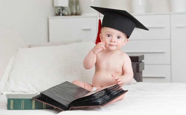 Portret van slimme babyjongen in afstudeerpet poseren met boeken