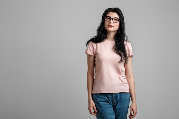 Portret van slimme mooie brunette meisje in brillen met natuurlijke make-up, op grijze achtergrond.