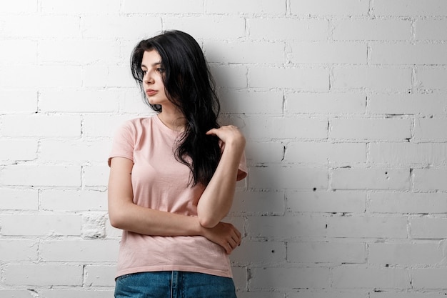 Portret van slimme mooie brunette meisje in brillen met natuurlijke make-up staande in de buurt van witte bakstenen muur.