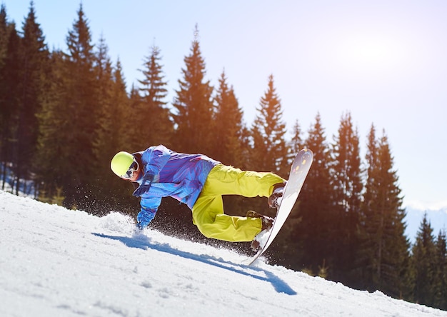 Portret van snowboarder die extreme truc doet tegen blauwe lucht en bossen op zonnige dag