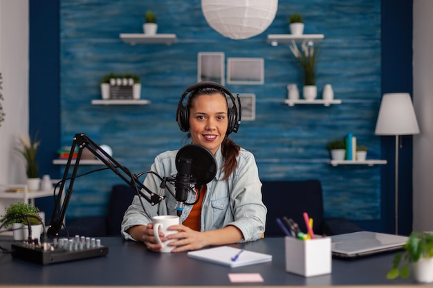 Portret van social media influencer met koptelefoon en streaming podcast. content creator-opname uitgezonden met koptelefoon en microfoon in thuiskantoor. lachende vrouw vlogger podcasting.