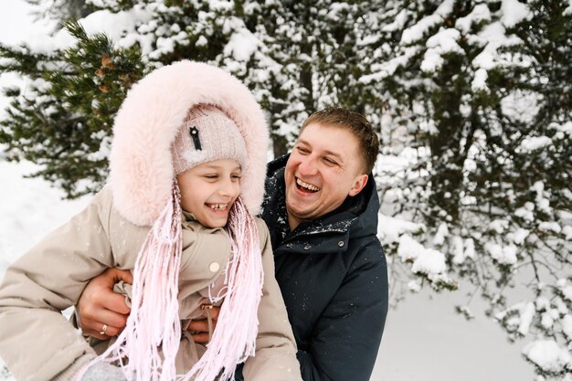 Portret van speelse gelukkige familie in winterbos. Vader en dochter knuffelen en spelen met sneeuw. Familieconcept. Genieten van tijd samen doorbrengen