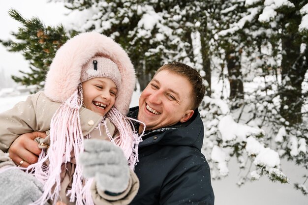 Portret van speelse gelukkige familie in winterbos. Vader en dochter knuffelen en spelen met sneeuw. Familieconcept. Genieten van tijd samen doorbrengen