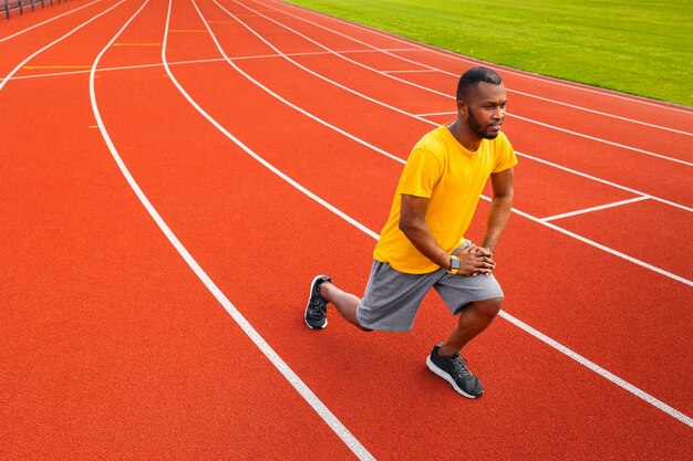 Portret van sportief gefocuste zwarte man in sportkleding die opwarmt voordat hij buiten traint in gele trendy sportkleding Jong Afro-Amerikaans lichaam dat zich uitstrekt op het stadionveld