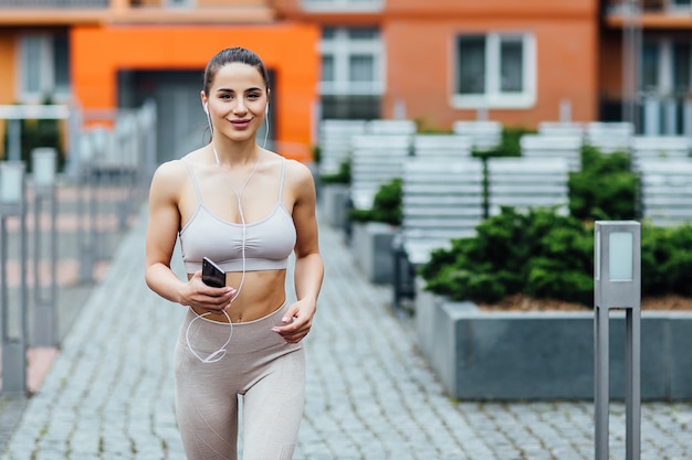 Portret van sterke atletische gelukkige sportvrouw die sportborrels dragen die sprong voorbereiden dichtbij huis.