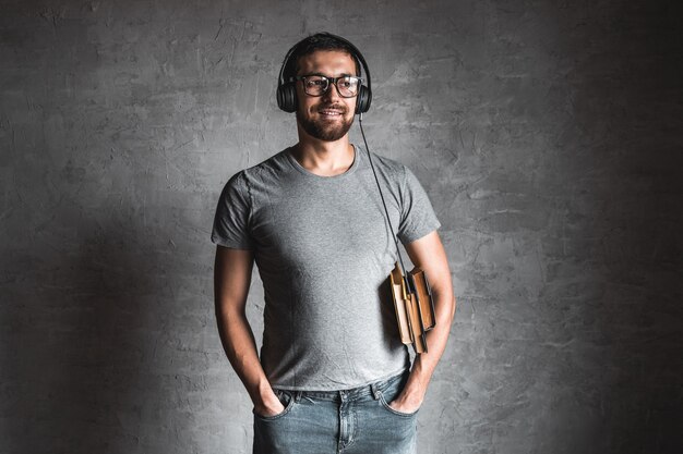 Portret van stijlvolle bebaarde man gekleed in grijs casual t-shirt luisteren audioboek met zijn koptelefoon en op de grijze achtergrond