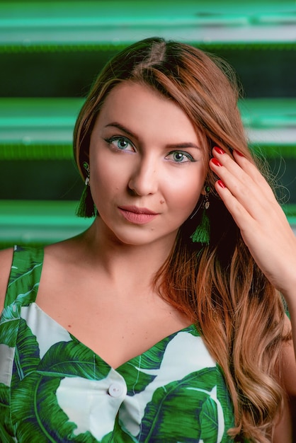 Portret van stijlvolle bruin haar vrouw in groene jurk groene oorbellen met make-up op groene achtergrond