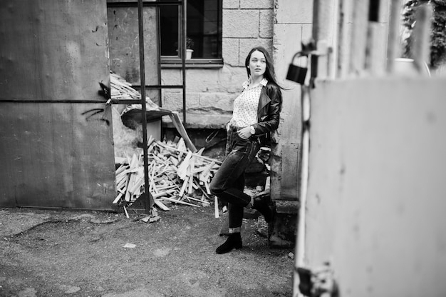 Portret van stijlvolle jonge vrouw die op leerjasje en gescheurde jeans in straten van stad draagt