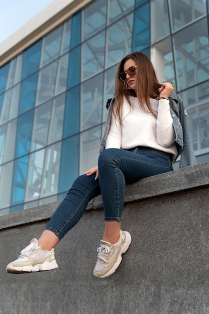 Portret van stijlvolle jonge vrouw in zonnebrillen op straat in de stad Aantrekkelijke vrouw rustend naast modern gebouw Verticaal