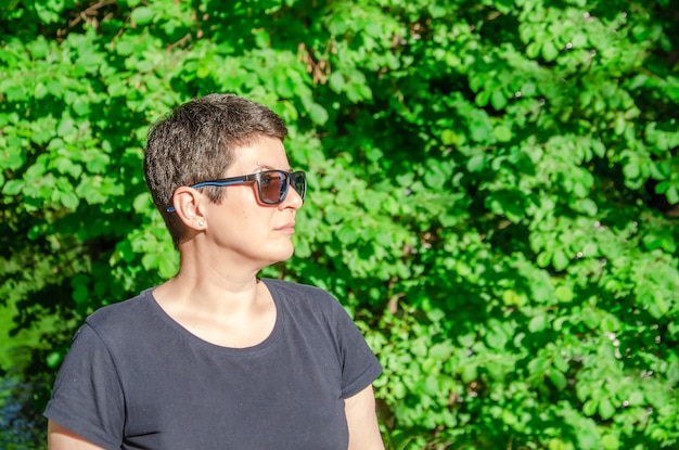 Portret van stijlvolle vrouw met zonnebril in profiel op zomerdag op groene natuurlijke achtergrond