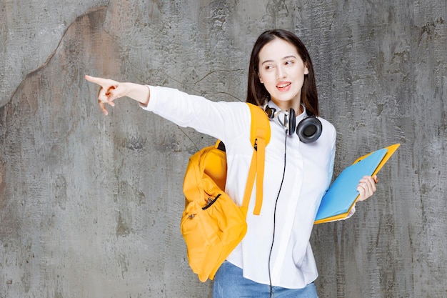 Portret van student met gele rugzak en boeken die ergens naar wijzen. Hoge kwaliteit foto