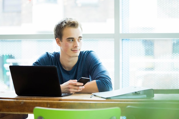 Portret van student met laptop en mobiele telefoon in een coffeeshop