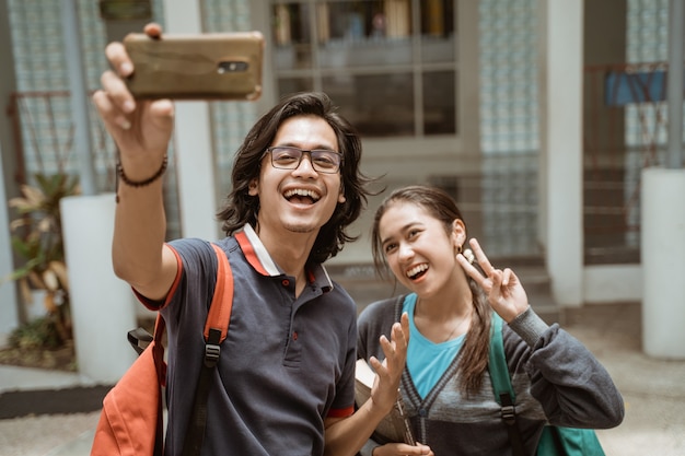 Portret van studenten erg blij en glimlachend nemen een selfie op de voortuin van de campus