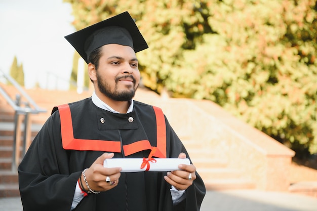 Portret van succesvolle Indiase student in afstudeerjurk duim omhoog