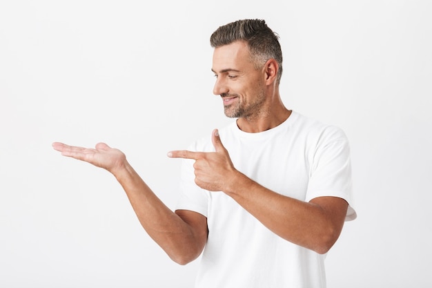 Portret van succesvolle man 30s met borstelharen dragen casual t-shirt wijzende vinger naar copyspace houden op palm geïsoleerd op wit