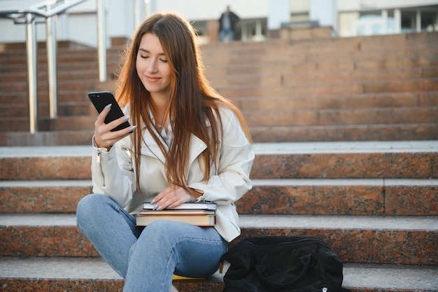 Portret van succesvolle student gelukkig tiener meisje poseren houden boeken glimlachen kijken naar Camera permanent in de buurt van moderne universiteitsgebouw buiten studentschap modern onderwijs