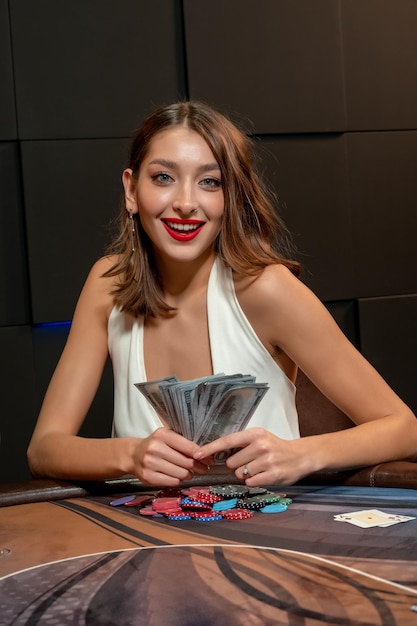 Portret van succesvolle vrouwelijke pokerspeler. gelukkig opgewonden jonge vrouw winnen in kaartspel in casino, zittend aan speeltafel met fan van bankbiljetten in handen. vrije tijd, levensstijl, gokconcept