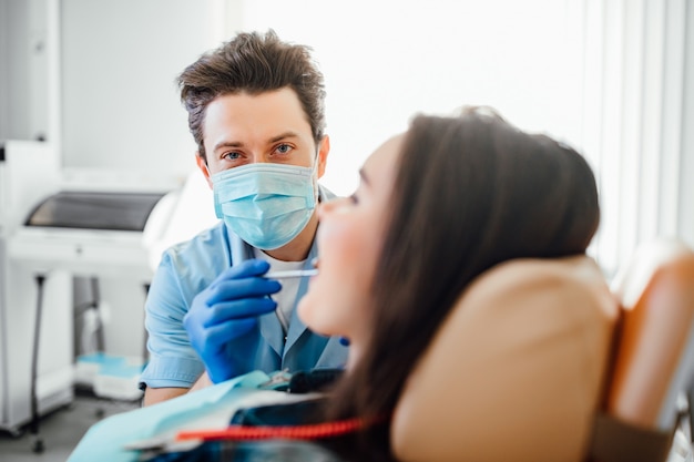 Portret van tandarts in blauw masker die met geduldige tanden in moderne kliniek werkt.