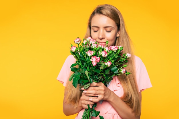 Portret van tedere aantrekkelijke blonde vrouw met groot boeket rozen geïsoleerd op gele achtergrond. Vakantie en geschenken concept. Vrouwendag. Valentijnsdag