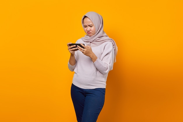 Portret van teleurgestelde jonge aziatische vrouw die videogame speelt op mobiele telefoon