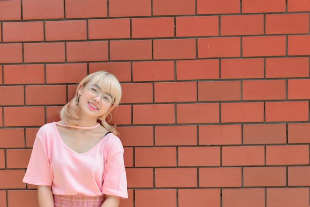 Portret van Thaise vrouw met gouden haren in japanse stijl op oranje bakstenen muur Aziatisch meisje poseert voor het maken van een foto buiten