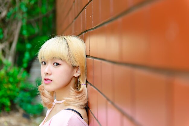 Portret van Thaise vrouw met gouden haren in japanse stijl op oranje bakstenen muur Aziatisch meisje poseert voor het maken van een foto buiten