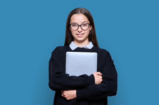 Portret van tiener vrouwelijke student met laptop camera kijken op blauwe kleur achtergrond Aantrekkelijke tiener meisje in glazen poseren in studio Middelbare school adolescentie studie onderwijs kennis