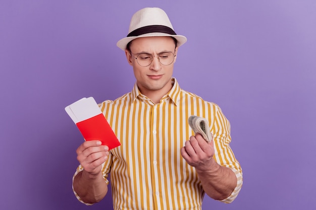 Portret van toeristische onzekere man houdt kaartjes contant bankbiljet vast, denk betaling op paarse achtergrond
