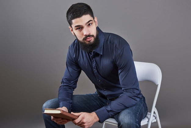 Portret van toothy knappe bebaarde man zittend op een stoel met boek over handen