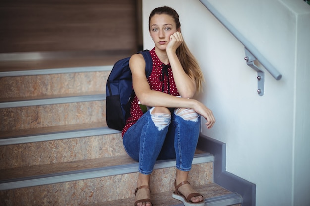 Portret van triest schoolmeisje zit alleen op trap