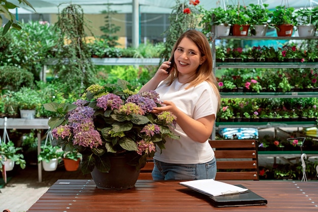 Portret van tuincentrummanager die met bloemen werkt en telefonisch praat